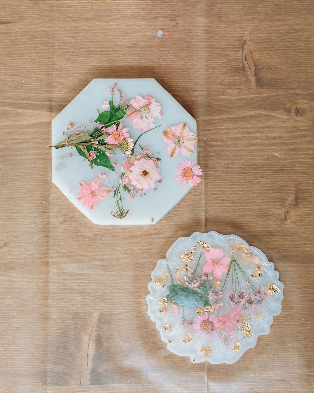 Two resin coasters with pink flowers set inside, on an oak table