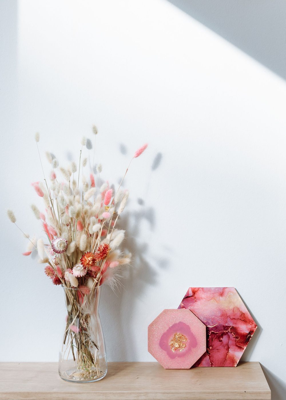 Pink resin hexagon coasters beside a vase of dried flowers